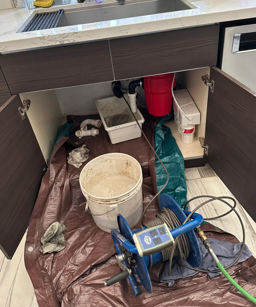 An open kitchen sink cabinet revealing a plumbing repair in progress
