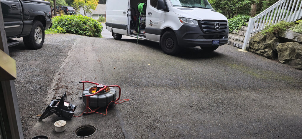 A white service van and plumbing equipment on an asphalt driveway