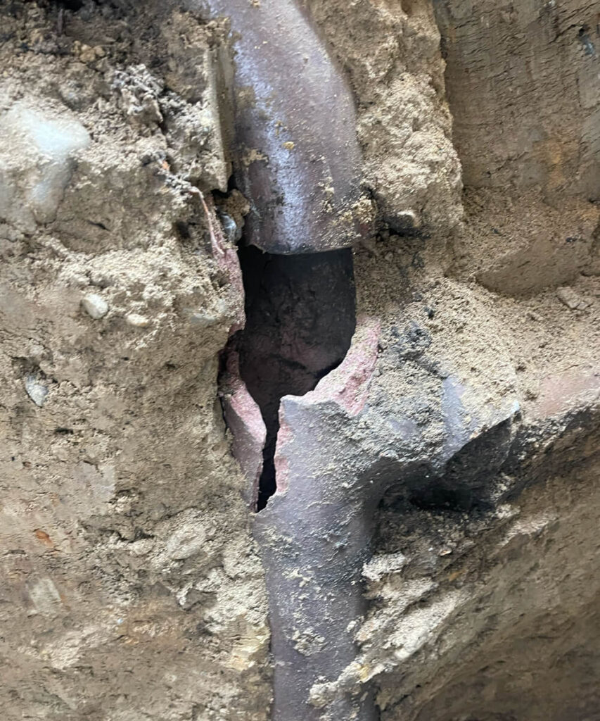 A severely cracked and broken underground pipe exposed in excavated soil